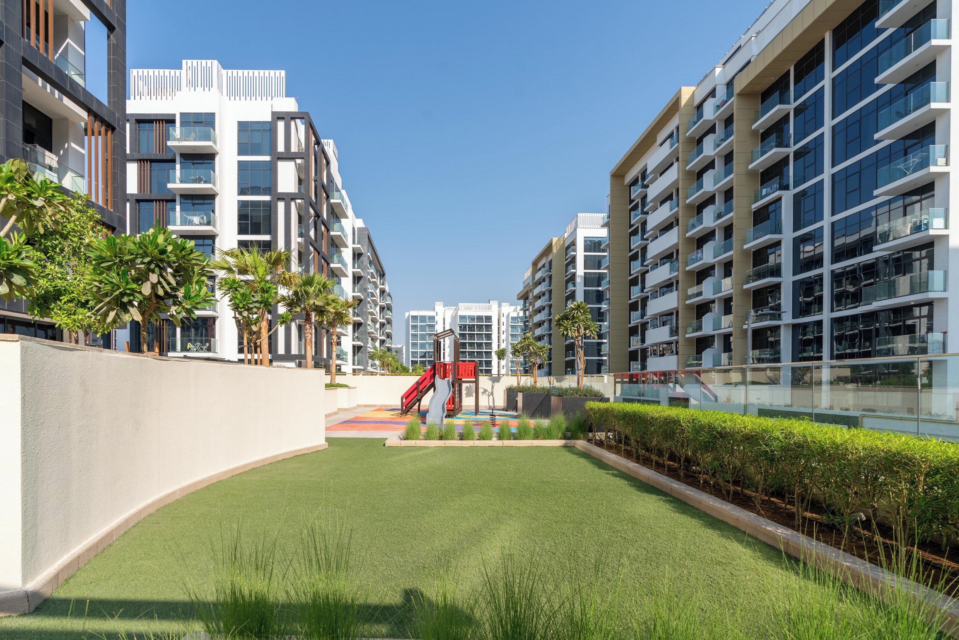 En moderne boligbygning med en central gårdsplads med kunstgræs, palmer og en legeplads.