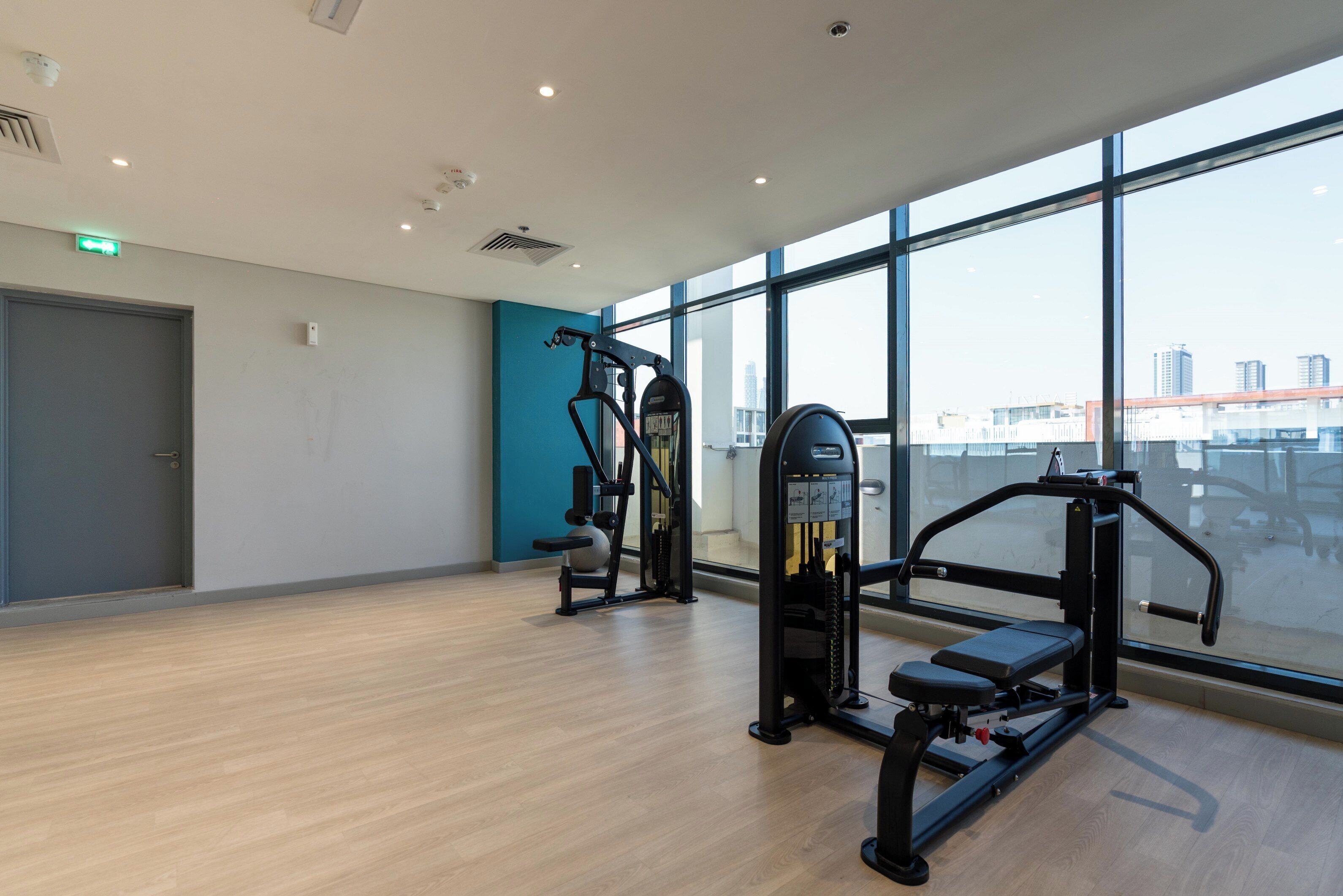 Une salle de sport spacieuse, dotée de grandes fenêtres, d’équipements d’exercice et d’un plancher en bois.