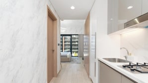 Een moderne keuken met een inbouwfornuis, gootsteen en kasten. Een gang leidt naar een slaapkamer met een groot raam en uitzicht op de omgeving.