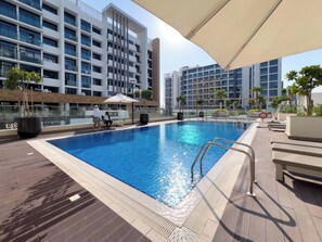 A rooftop pool with a clear blue water surface, surrounded by modern buildings and a few potted plants.