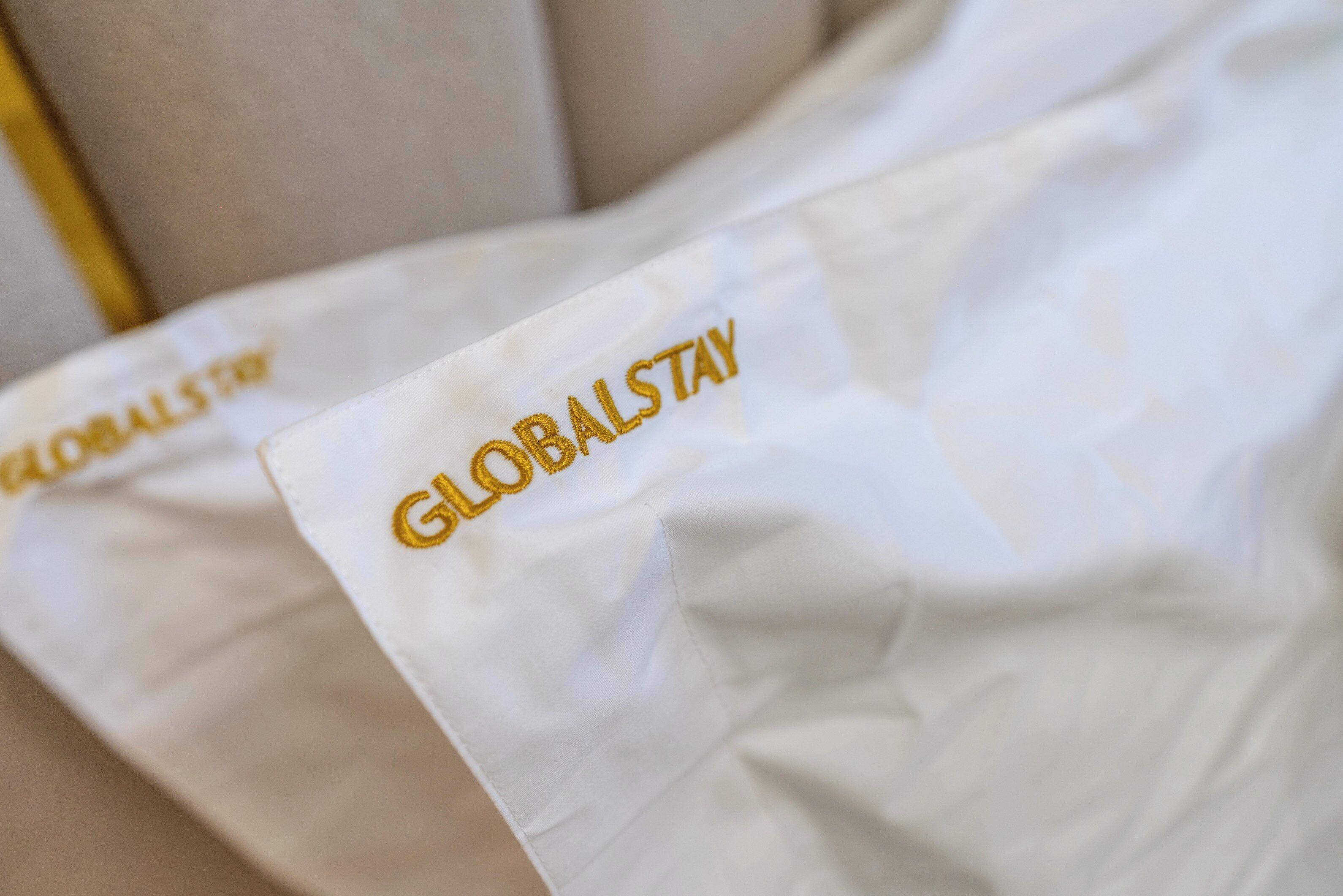 Een witte stof met “GLOBALSTAY” in goud geborduurd.
