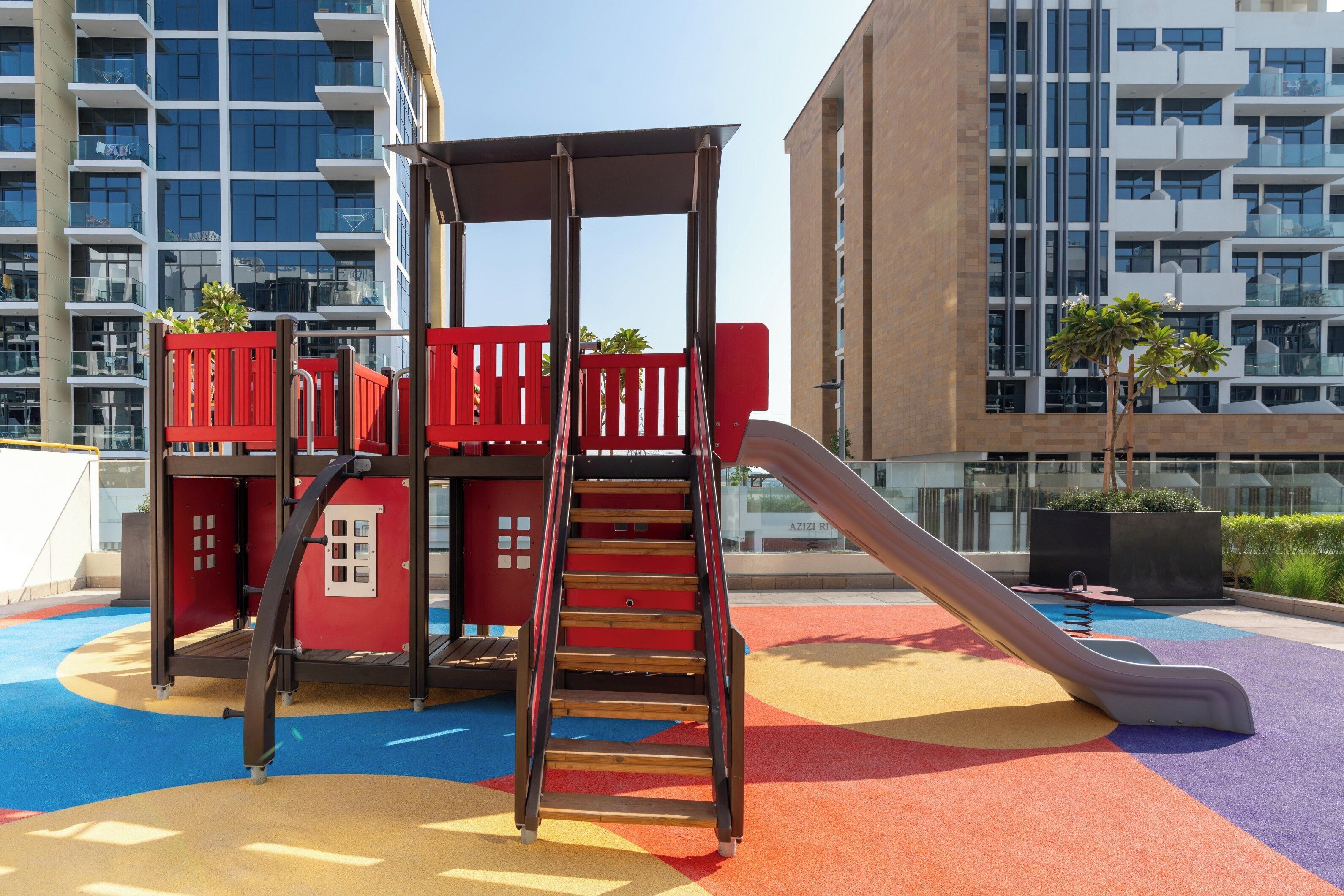 Un parque infantil con un tobogán y una estructura para escalar, rodeado de edificios.