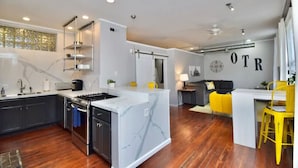 Een moderne keuken met een marmeren eiland, een ingebouwde oven en een eethoek met gele stoelen.