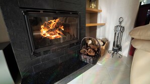 A fireplace with a fire, a basket of pinecones, and a candle holder on a tiled floor. - Private Pool and Hot Tub on the Douro River (São Lourenço do Douro)