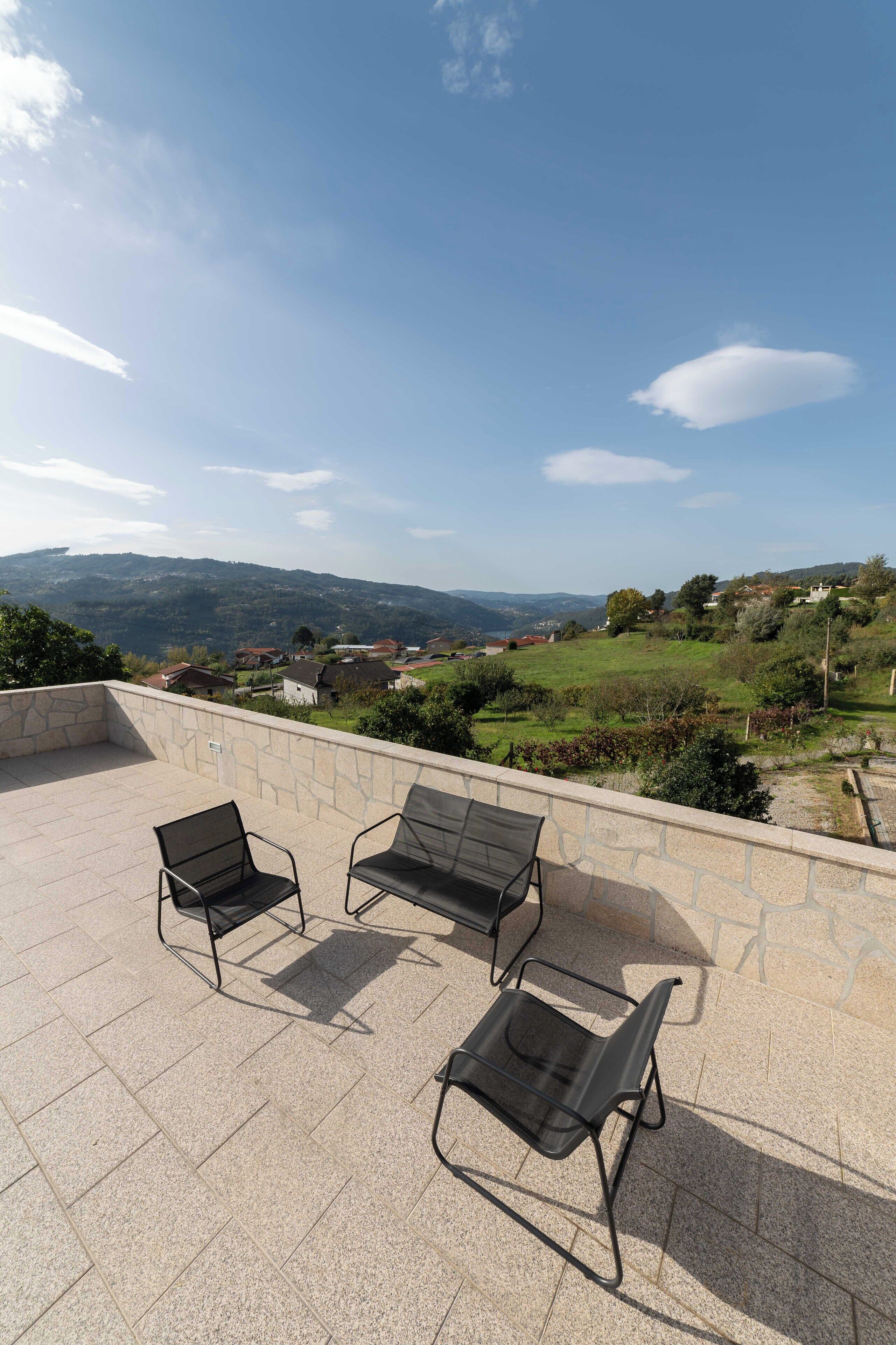 A terrace with three black metal chairs and a stone wall.