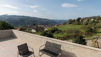 A terrace with three black metal chairs and a stone wall.