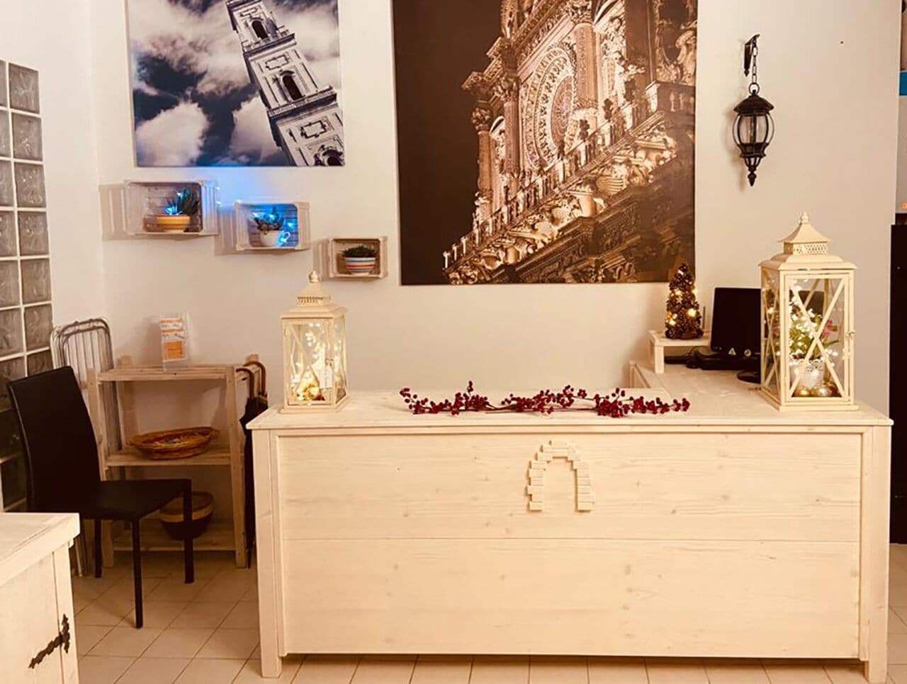 Una habitación con un aparador de madera, una silla, una mesita con una cesta, y una pared con un cuadro grande enmarco y dos faroles colgantes.