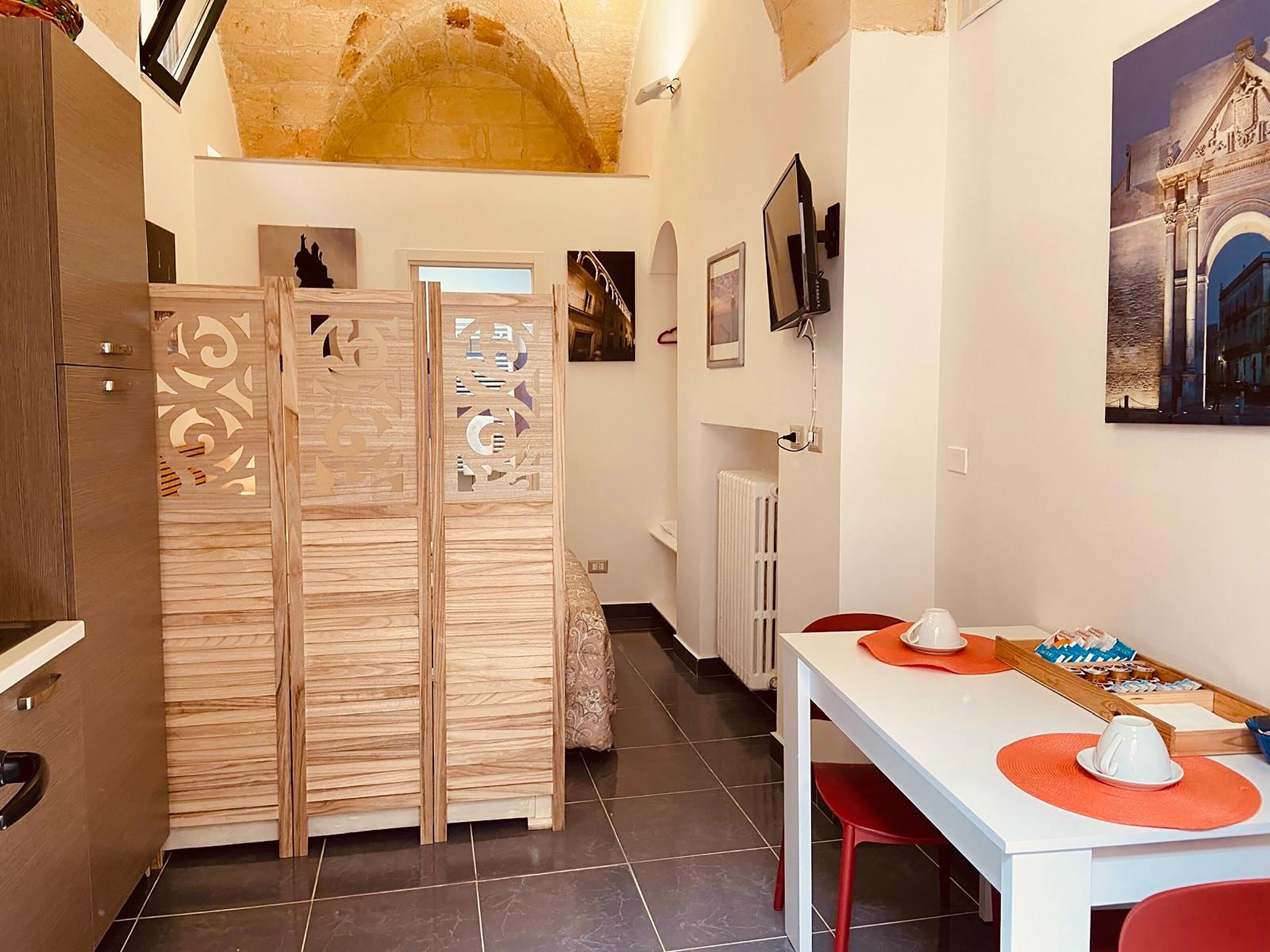 Una cocina compacta con un armario de madera, una mesa blanca con sillas rojas y un radiador.