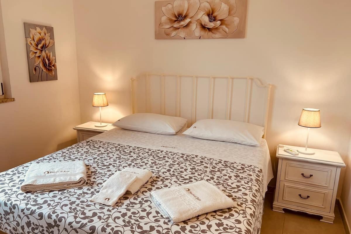 A neatly made bed with a patterned bedspread, two pillows, and two bedside lamps. There are two folded towels on the bed.