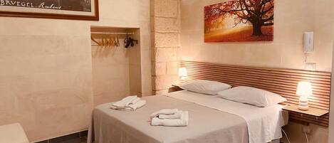 Una habitación de hotel con una cama grande, cabecera, dos mesitas de noche con lámparas, un cuadro de un árbol y un marco con una fotografía en la pared.