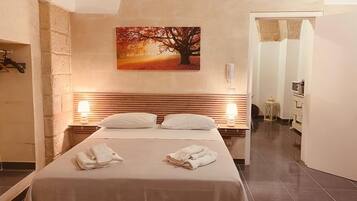 A hotel room with a bed, two bedside lamps, a painting of a tree, and a bathroom visible through an open door.
