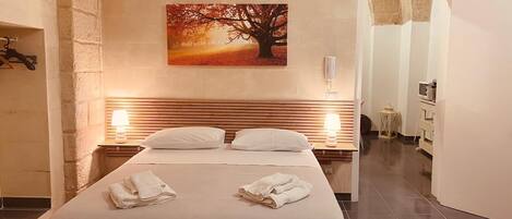 A hotel room with a bed, two bedside lamps, a painting of a tree, and a bathroom visible through an open door.