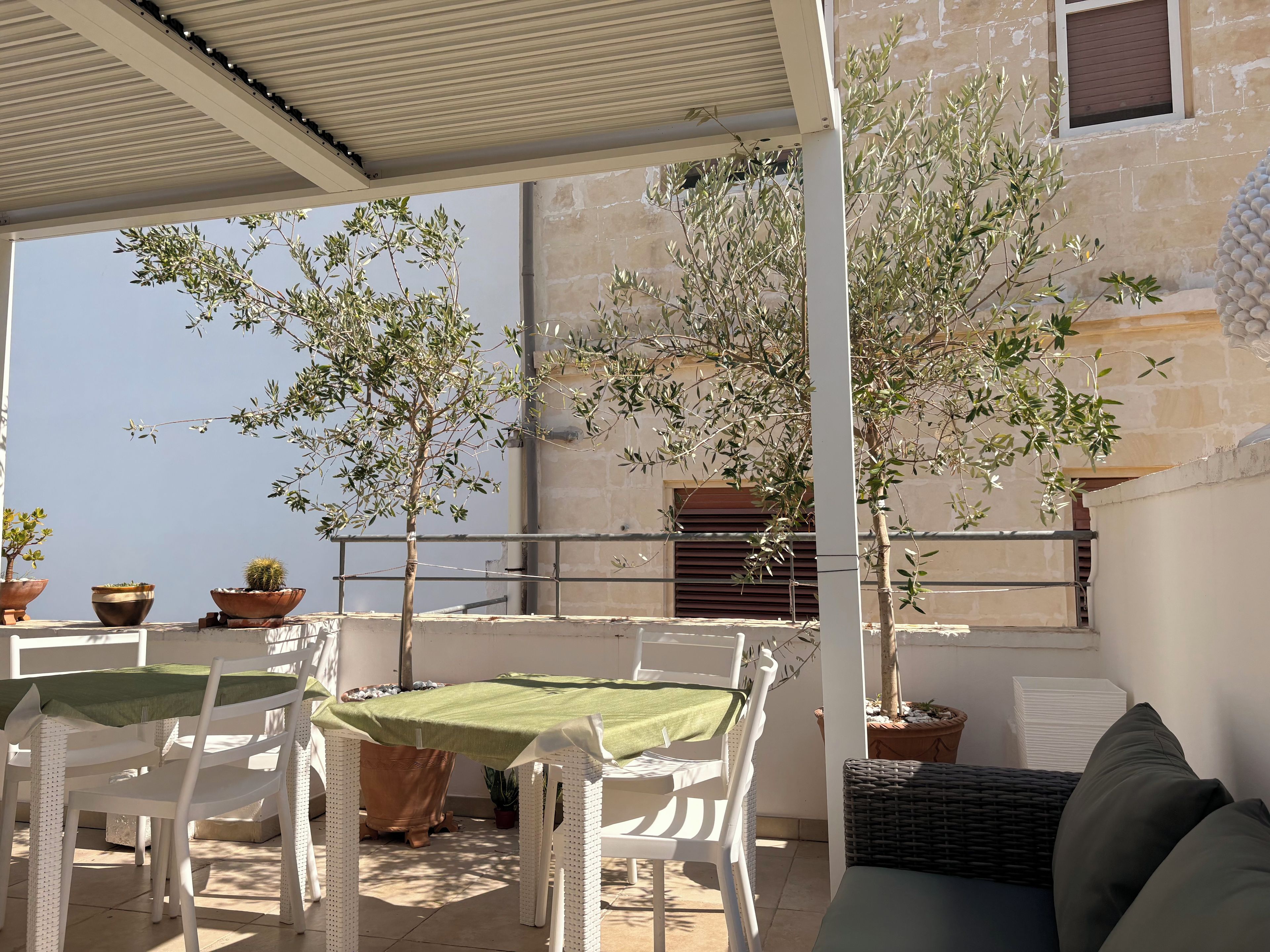 An outdoor seating area with a table and chairs, surrounded by potted plants and a building in the background.