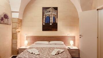 Une chambre d’hôtel avec un grand lit, une table de chevet, une lampe et un tableau représentant un bâtiment accroché au mur.