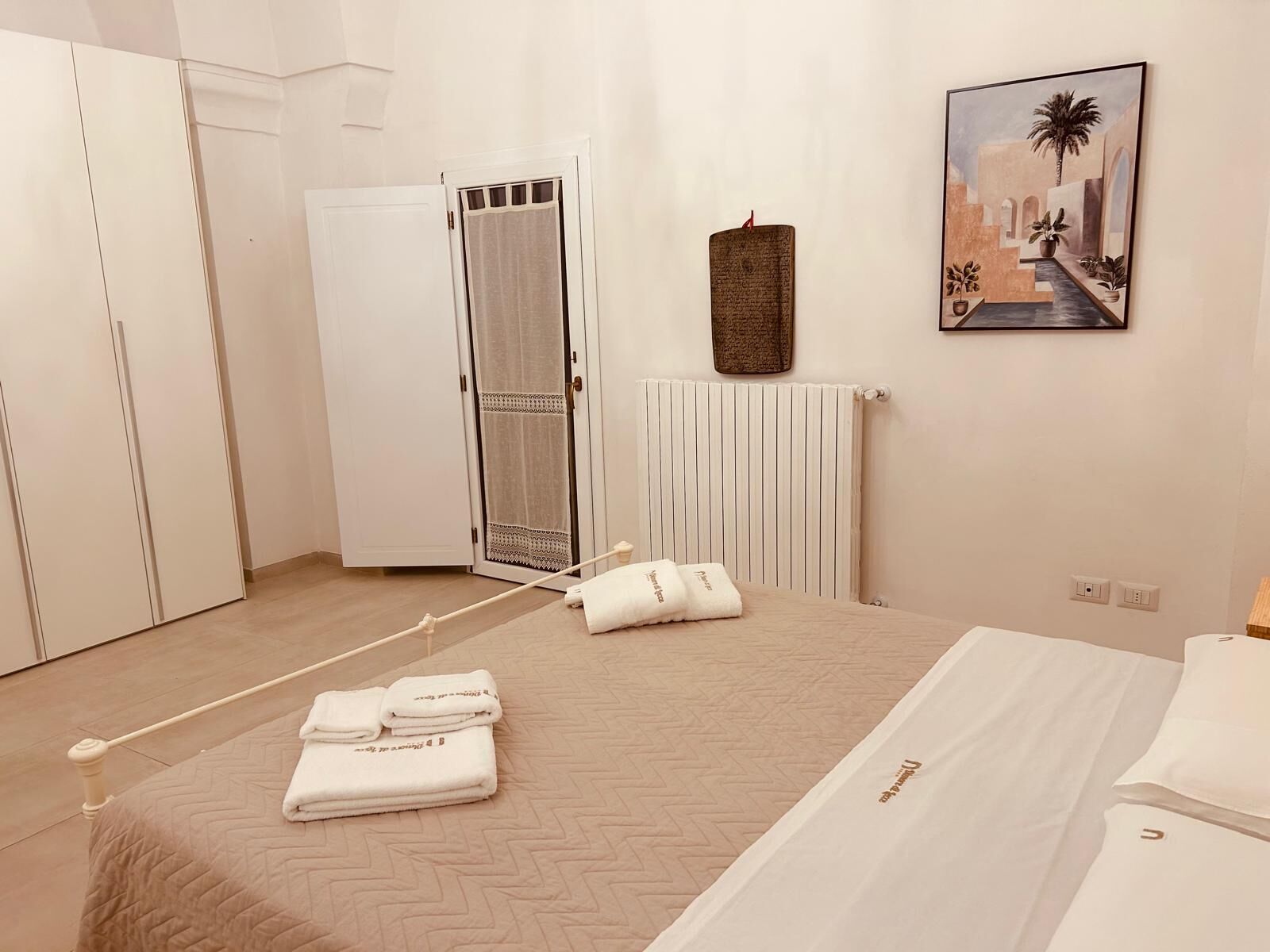 Ein Schlafzimmer mit einem Bett, einem Heizkörper, einer Tür mit Vorhang und einem Bild an der Wand.