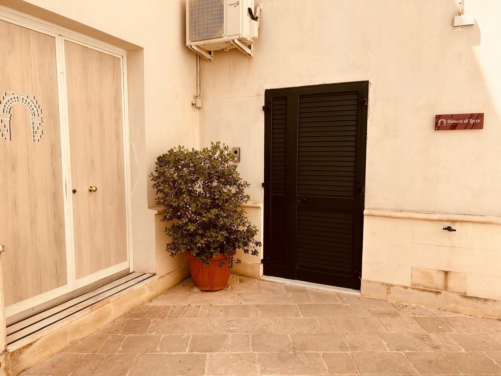 A building with a large wooden door, a black shutter door, and a potted plant in the entrance.