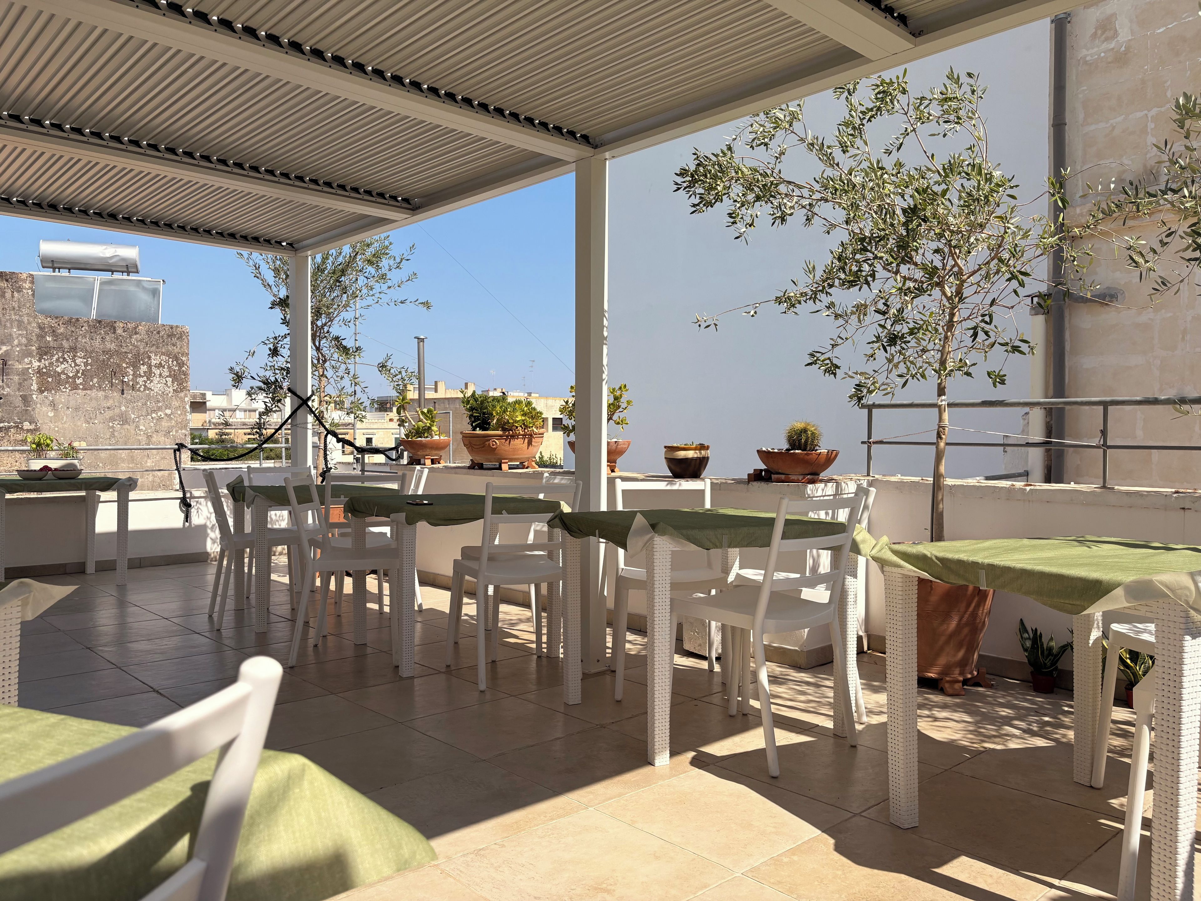 An outdoor patio with white wicker furniture, green tablecloths, and potted plants.