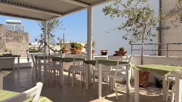 An outdoor patio with white wicker furniture, green tablecloths, and potted plants.