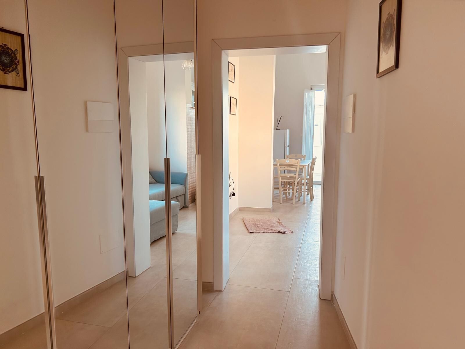 A hallway leading to a dining area with a table and chairs, a sofa, and a rug on the floor.
