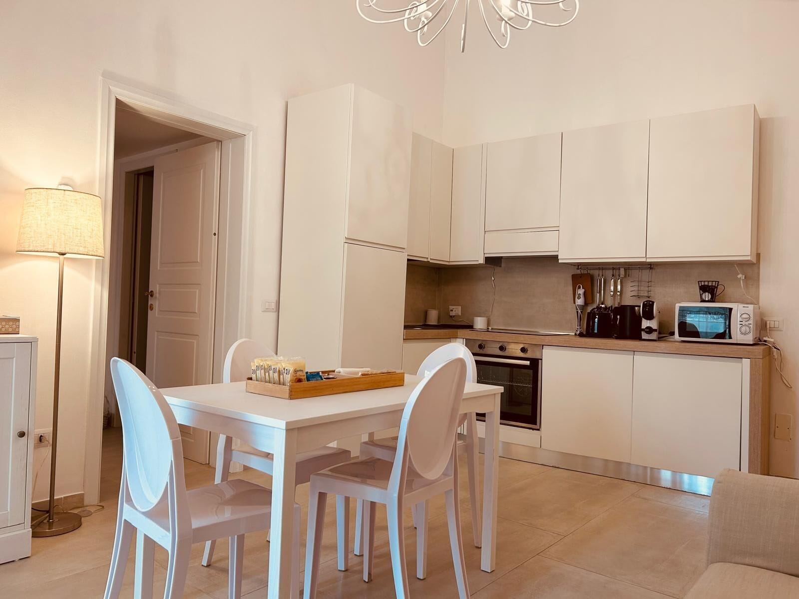 A compact kitchen with white cabinets, a microwave, a kettle, and a dining table with chairs.