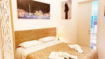 A hotel room with a bed, a night view painting, a statue, and a door leading to a balcony.