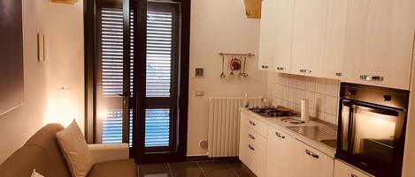 Una cocina moderna con armarios blancos, estufa a gas y horno empotrado. En la zona de estar contigua hay un sofá con cojines.