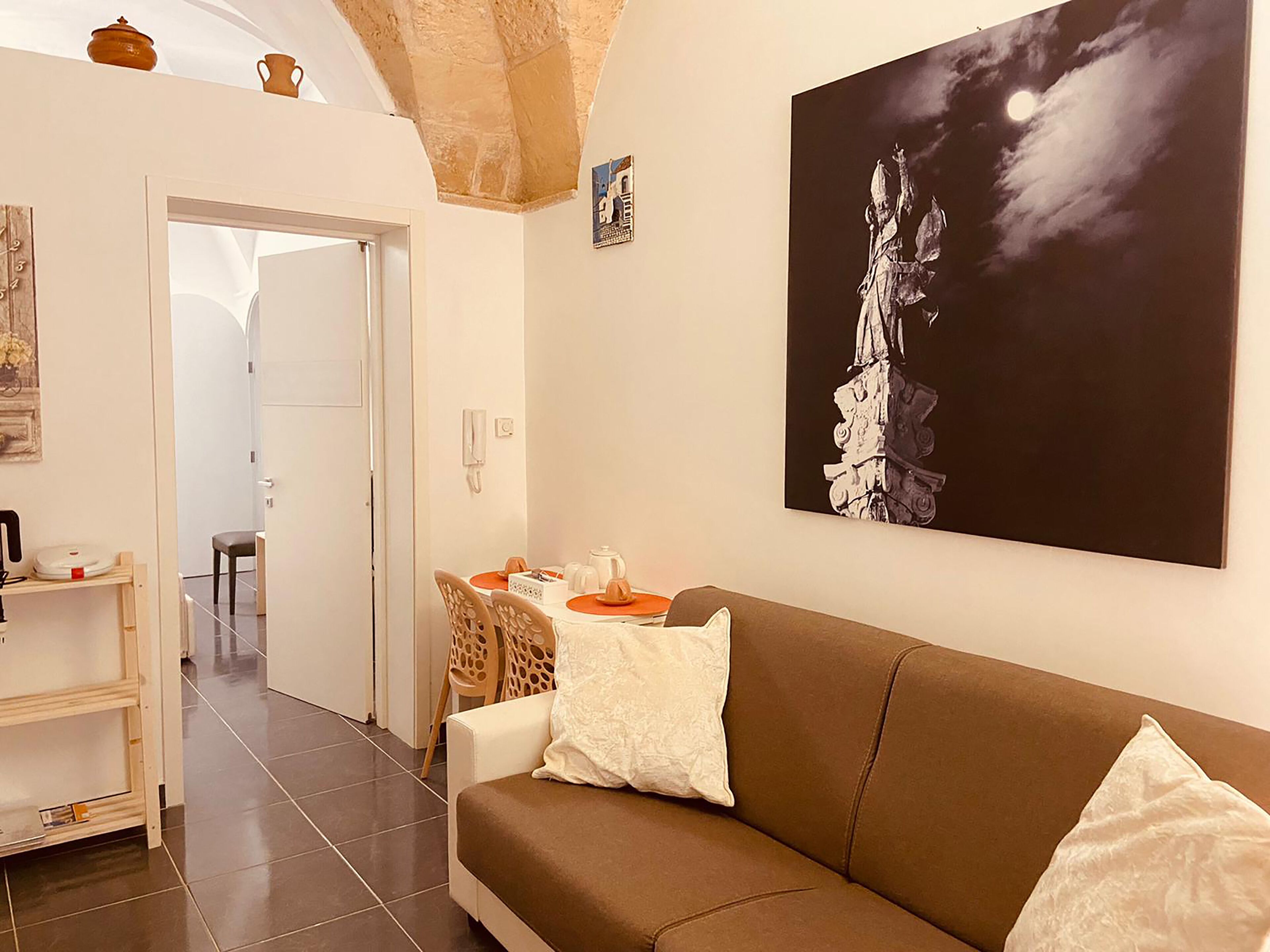 A modern living room with a brown sofa, a white pillow, and a framed artwork of a tree against a night sky.