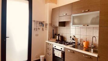 A compact kitchen with a stove, oven, microwave, and sink. There are cabinets and a small trash bin.