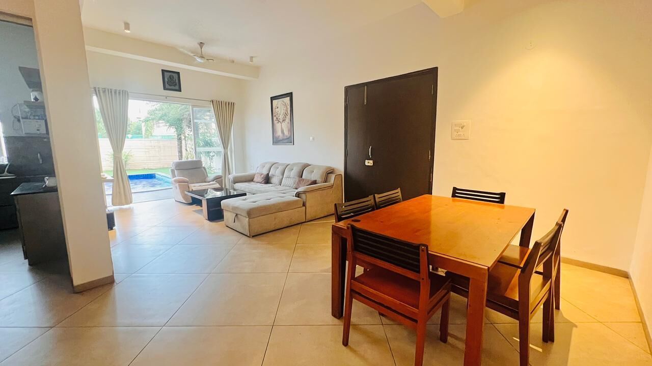 A living room with a sofa, a dining table with chairs, a kitchen area, and a sliding glass door leading to an outdoor space.