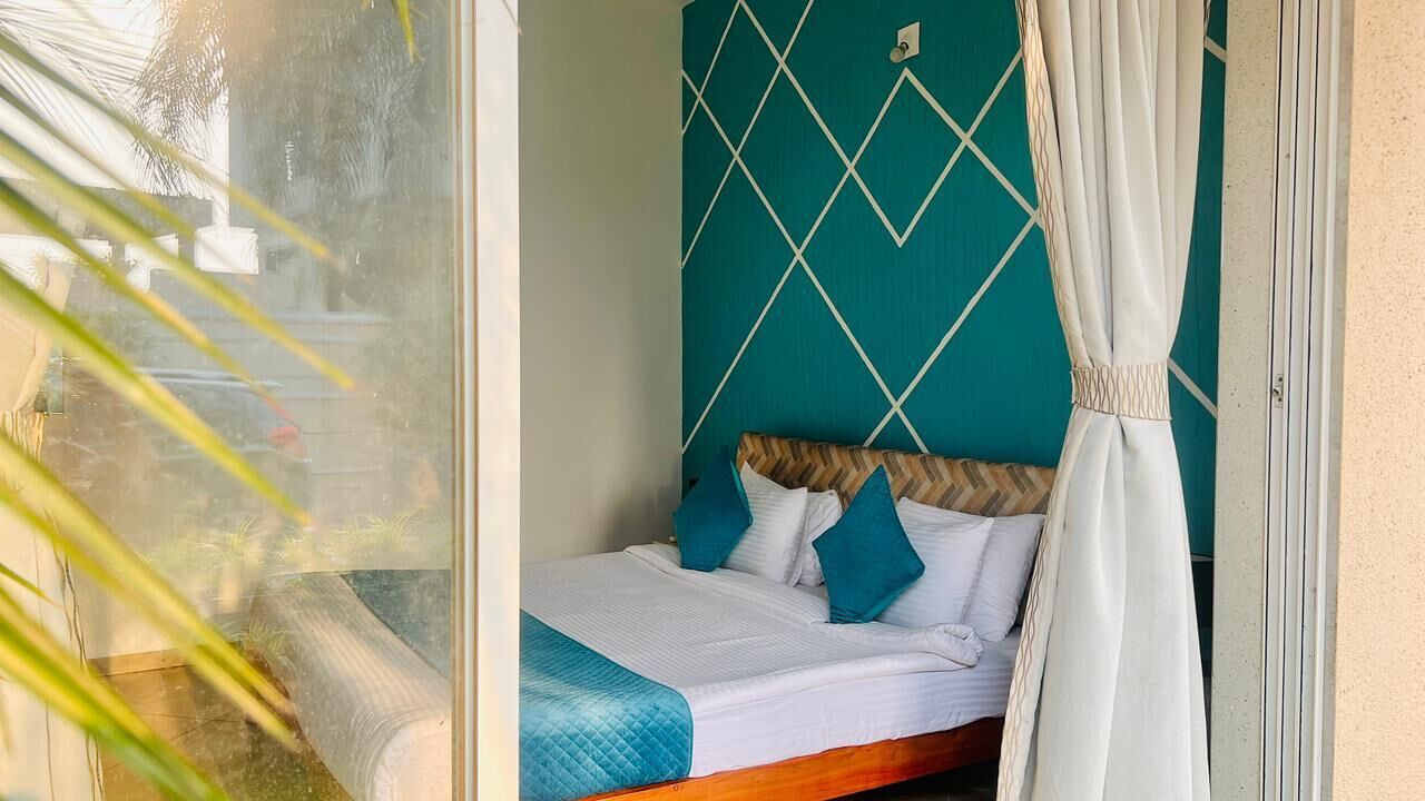 A room with a bed, white curtains, and a teal wall with a diamond pattern.
