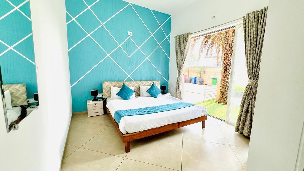 A bedroom with a bed, bedside tables, a mirror, and a view of the outside.