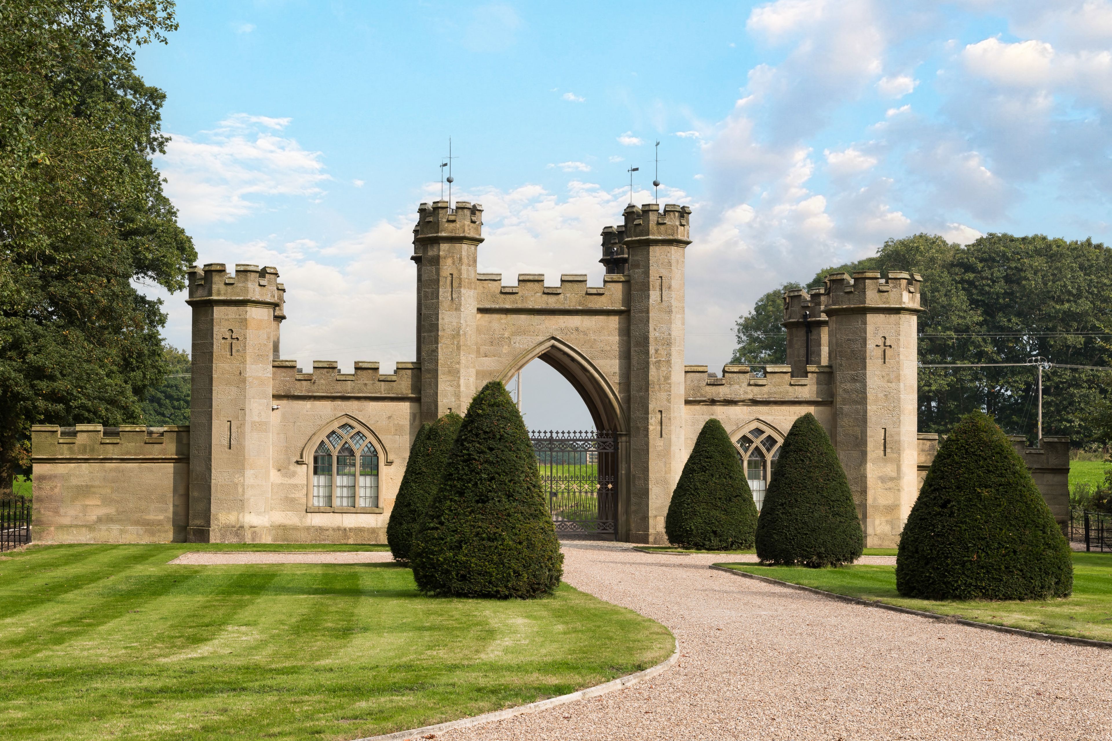 A castle entrance with a gravel path, a large archway, and symmetrical towers.