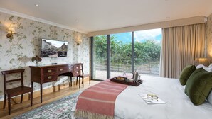 A bedroom with a large bed, a desk, and a chair. There is a window with a view of trees and buildings. - Bryngwilla Gate Lodge - Oswestry , Shropshire (Oswestry)