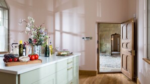 A kitchen with a white countertop, a wooden cutting board with fruits and vegetables, and a vase with flowers. - Bryngwilla Gate Lodge - Oswestry , Shropshire (Oswestry)