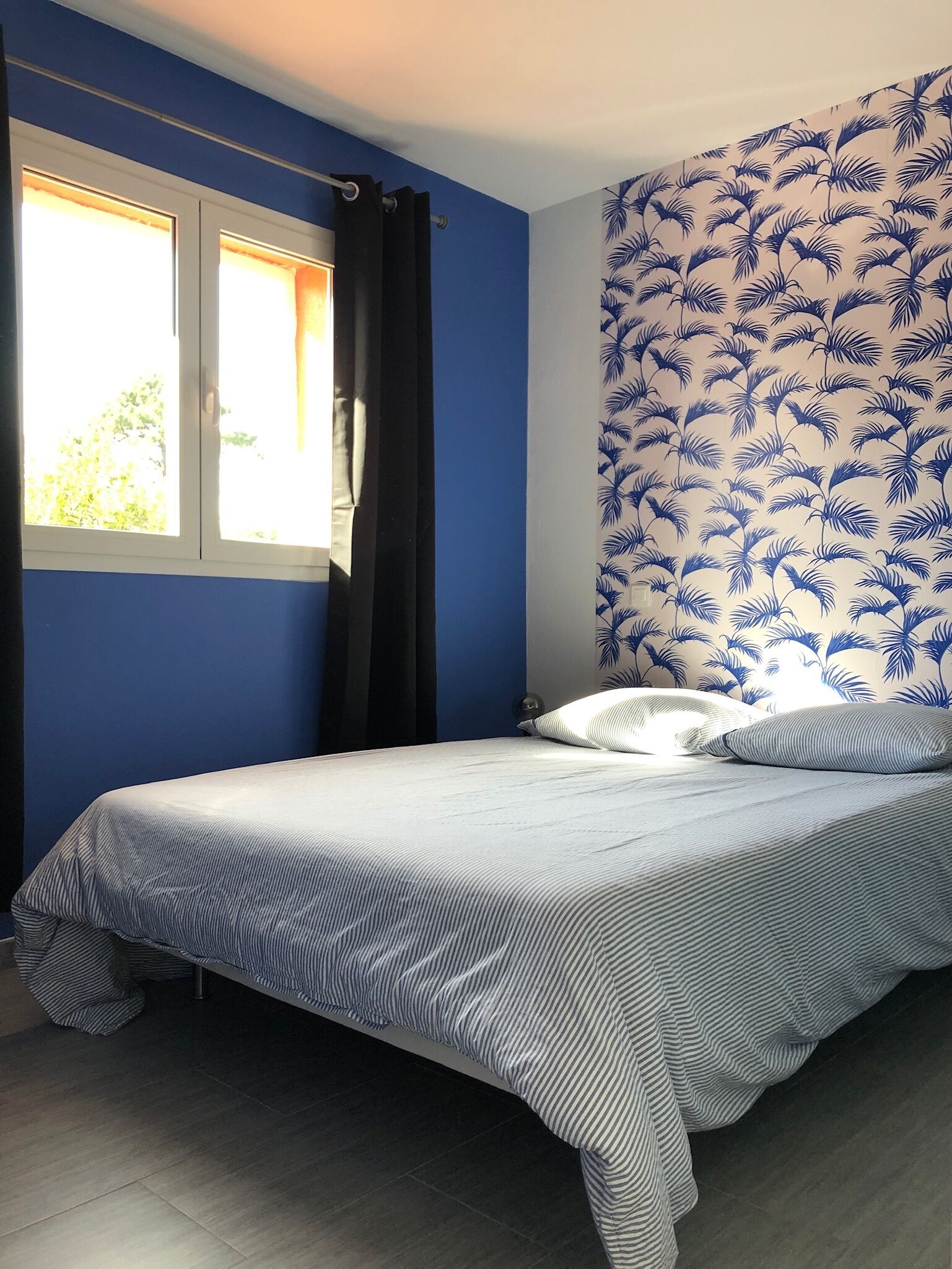 A bedroom with a bed, curtains, and a patterned wall.