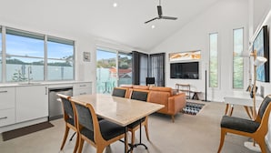 A modern kitchen with a dining area, a sofa, and a TV. - White Beach - Whole Property (Terrigal)