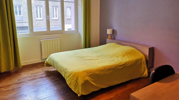 Een slaapkamer met een bed, een raam, een radiator en een lamp.