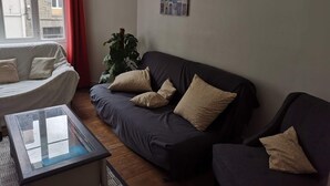 Een woonkamer met een donkere bank, twee fauteuils, een glazen salontafel en een potplant.