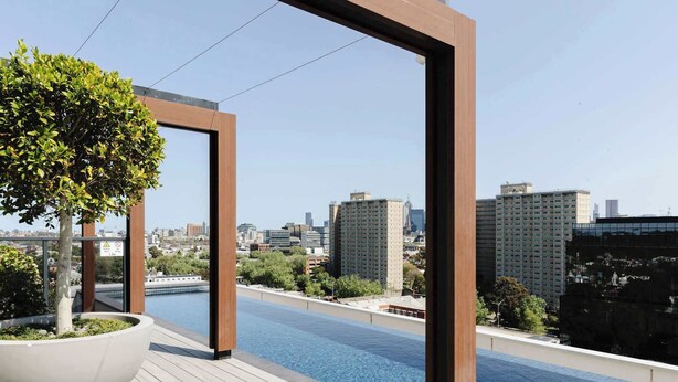 A rooftop pool with a city view, surrounded by wooden decking and a large planter with a tree. - Abbotsford Abode With Pool, Parking & Gym (Abbotsford)