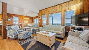 A cozy living room with wooden paneling, a sofa, two armchairs, a coffee table, and a television. - Summer Days 4 Bedroom Oceanfront Home (Kill Devil Hills)