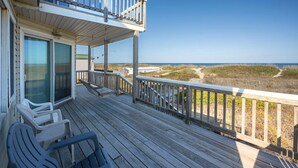A wooden deck with chairs and a railing overlooking a beach. - Summer Days 4 Bedroom Oceanfront Home (Kill Devil Hills)