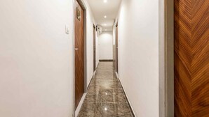 A hallway with a marble floor, white walls, and wooden doors. - HOTEL METROMAX (Mumbai)