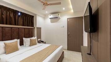 Une chambre d’hôtel équipée d’un lit, d’un ventilateur de plafond, d’un climatiseur, d’un téléviseur fixé au mur et d’une armoire en bois.