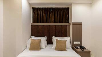 A hotel room with a bed, two pillows, a nightstand with a phone, and a brown headboard.