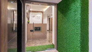 A modern hotel entrance with a glass door, a green artificial grass wall, and a decorative wall panel. - HOTEL METROMAX (Mumbai)