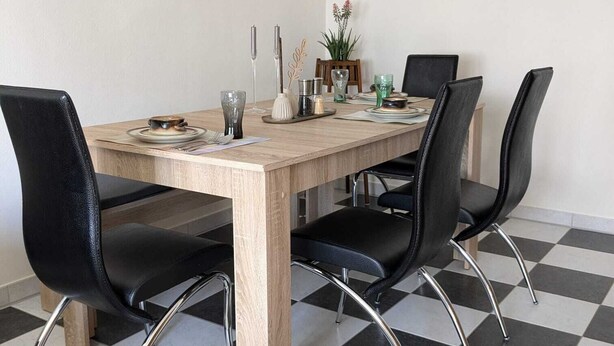 Un espace repas avec une table en bois, des chaises en cuir noir et un sol à carreaux.
