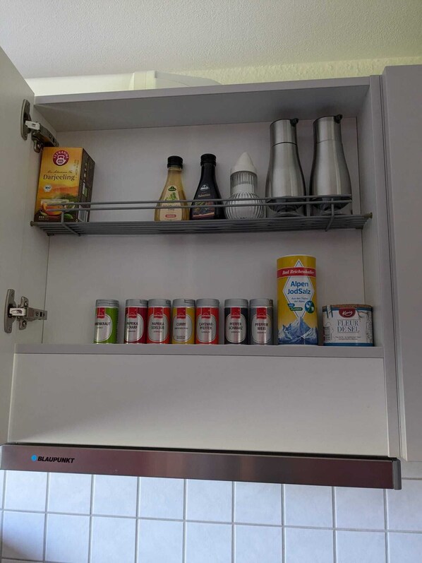 A kitchen cabinet with shelves holding various kitchen items including spices, condiments, and a box of Darjeeling tea.