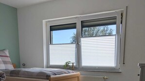 Une chambre à coucher avec un lit, un radiateur, une fenêtre avec des stores et une commode.