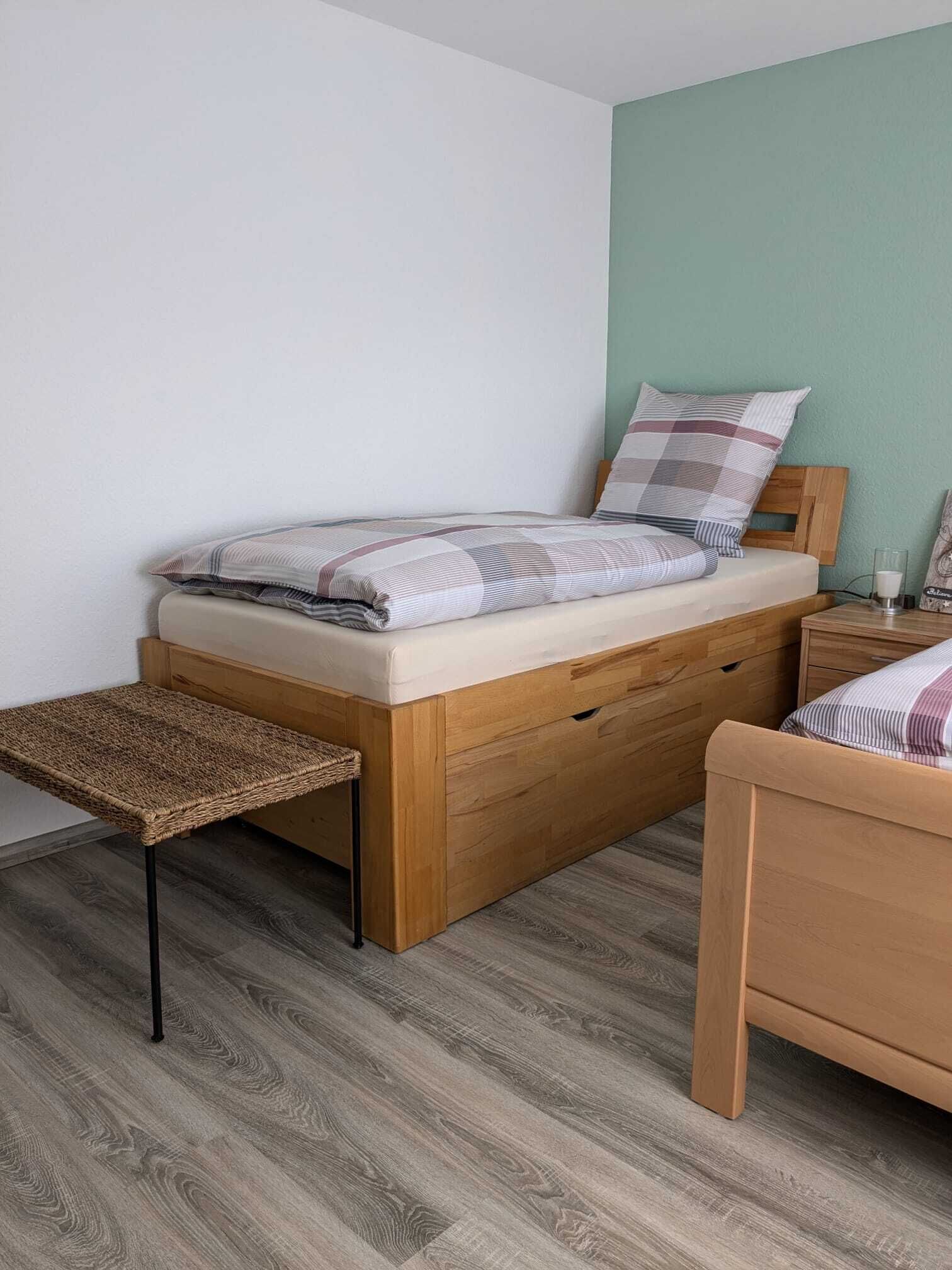 Un dormitorio con una cama de madera, una mesita de noche, un pequeño banco y una pared verde.