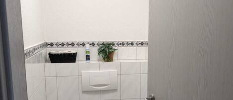 Un baño pequeño con inodoro, radiador, escoba y una planta en maceta.